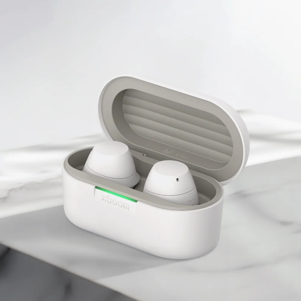 LG XBOOM 버즈 화이트 모델의 무선 이어폰 케이스가 열려 있는 모습입니다. 둥근 형태의 케이스는 흰색이며, 케이스 안에는 두 개의 흰색 이어폰이 자리하고 있습니다. 케이스 앞쪽에는 녹색으로 켜진 작은 LED 불빛이 보입니다. 밝은 색의 배경 위에 케이스가 정중앙에 배치되어 있습니다.