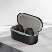 LG XBOOM 버즈 블랙 모델의 무선 이어폰 케이스가 열려 있는 모습입니다. 둥근 형태의 케이스는 검은색이며, 케이스 안에는 두 개의 검은색 이어폰이 자리하고 있습니다. 케이스 앞쪽에는 녹색으로 켜진 작은 LED 불빛이 보입니다. 밝은 색의 배경 위에 케이스가 정중앙에 배치되어 있습니다.