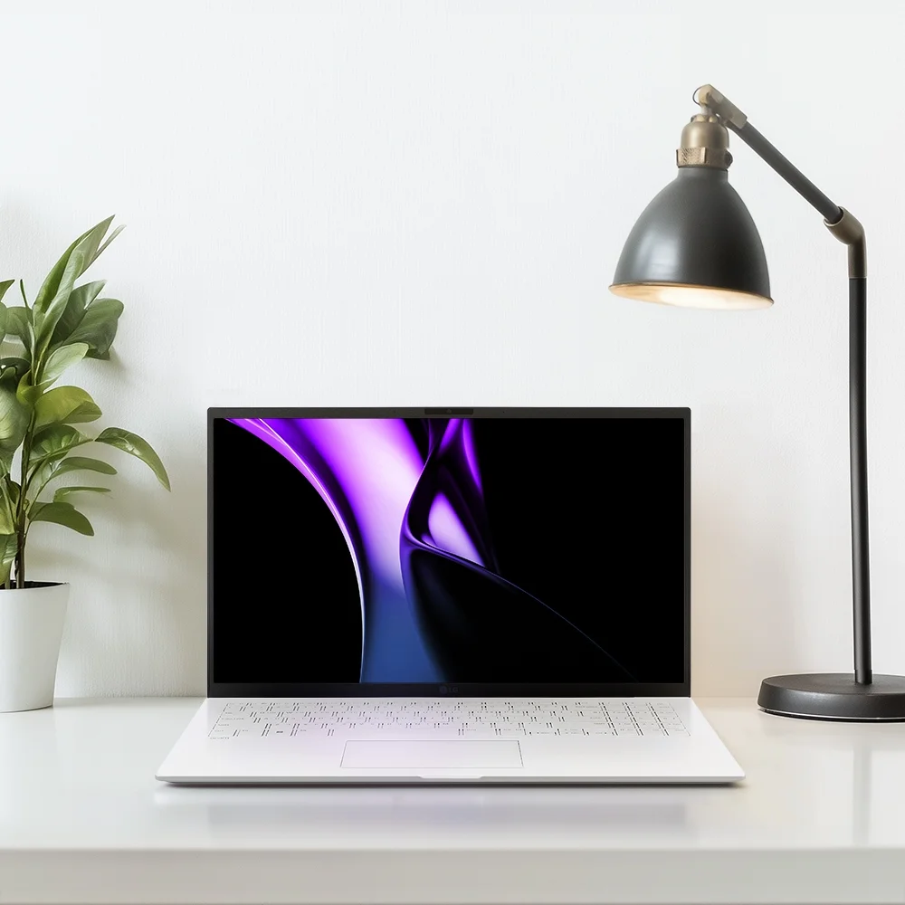 LG 그램 39.6cm 15Z90S 화이트 컬러 모델의 라이프 스타일 컷입니다. 하얀 책상 위에 노트북이 올려져 있고, 왼쪽에는 화분, 오른쪽에는 검은 색의 전등이 있습니다.