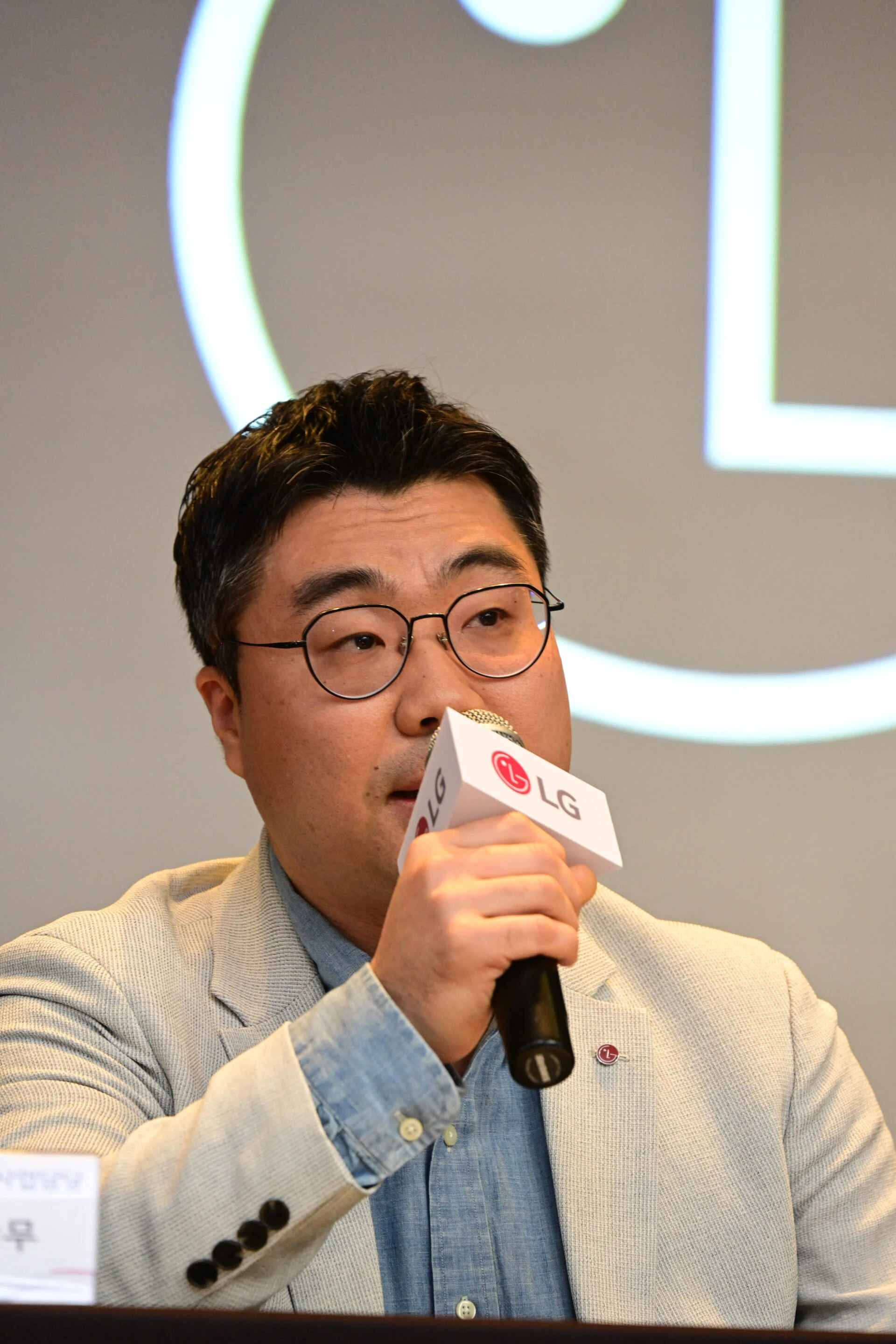 LG전자 스마트팩토리사업담당 송시용 상무가 마이크를 들고 발표 중인 모습. 그는 안경을 착용하고 연한 색의 재킷과 청색 셔츠를 입고 있으며, 진지한 표정으로 발언하고 있다.