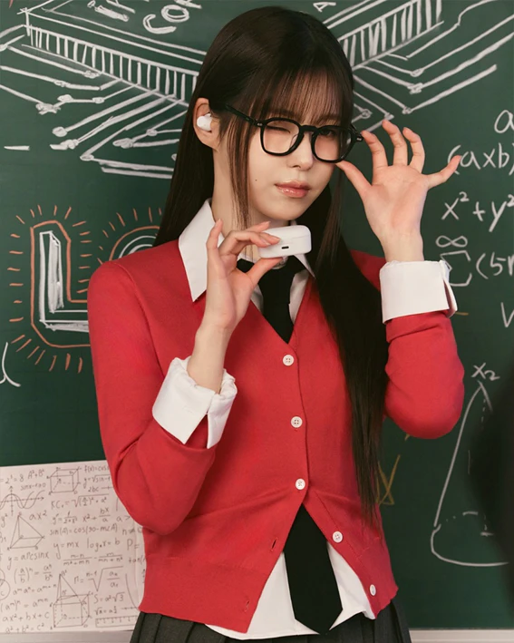 LG전자의 제품 사용 경험 소통 커뮤니티 ‘재미(Jammy)’의 브랜드 모델 ‘NMIXX 규진‘이 LG 엑스붐 버즈를 착용하고 있다. 붉은색 카디건과 넥타이를 착용한 긴 생머리 여성이 한 손에는 무선 이어폰 충전 케이스를 들고, 다른 손으로는 안경을 고쳐 쓰며 윙크하고 있다. 배경에는 회로도와 수학 공식이 그려진 초록색 칠판이 보인다.