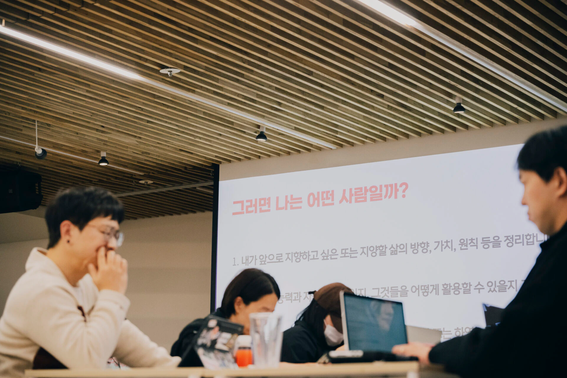 스토리소사이어티와 무의가 함께 진행한 볼드 무브 커뮤니티 현장. 컨퍼런스룸에서 여러 명이 강의를 듣고 있다. 스크린에는 '그러면 나는 어떤 사람일까?'라는 질문이 띄워져 있고, 한 참가자는 턱을 괸 채 집중하고 있다.