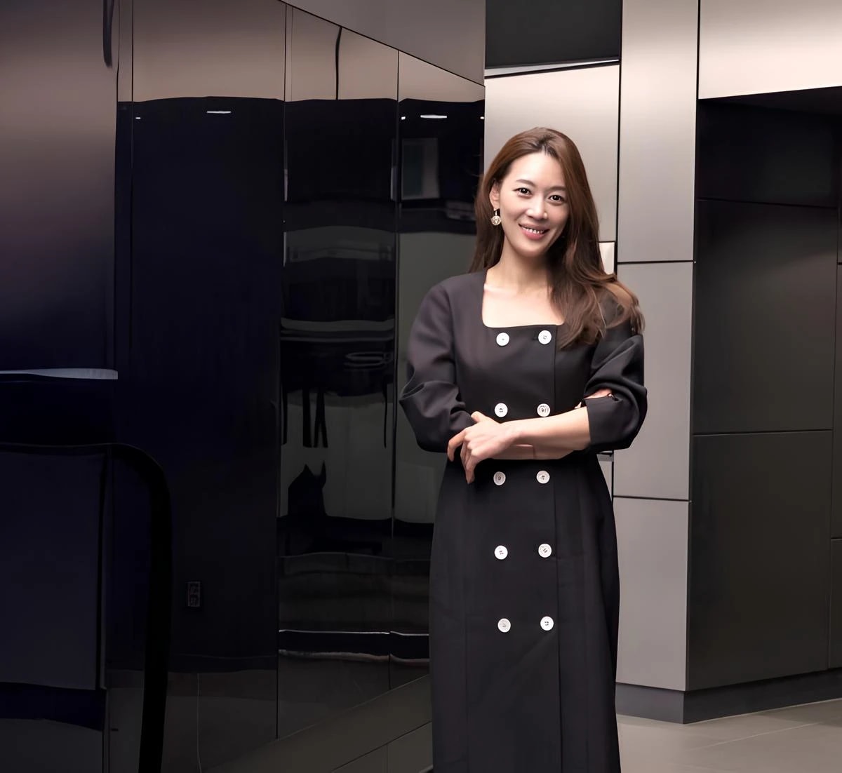 어두운 색 유광 패널이 배치된 실내 공간에서, 검은색 원피스를 입은 LG전자 김수연 상무/연구소장이 두 팔을 가볍게 포개고 서 있으며 카메라를 향해 미소 짓고 있다.